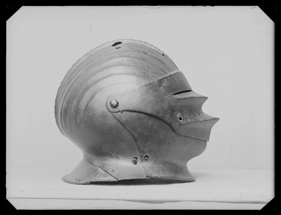 Sluten hjälm. Stilmässigt av tysk sk maximiliantyp, ca 1500-talets första hälft. Visir, hakstycke och nackskärm troligen senare kompletteringar, möjligen är även hjälmklockan 1800-tal.